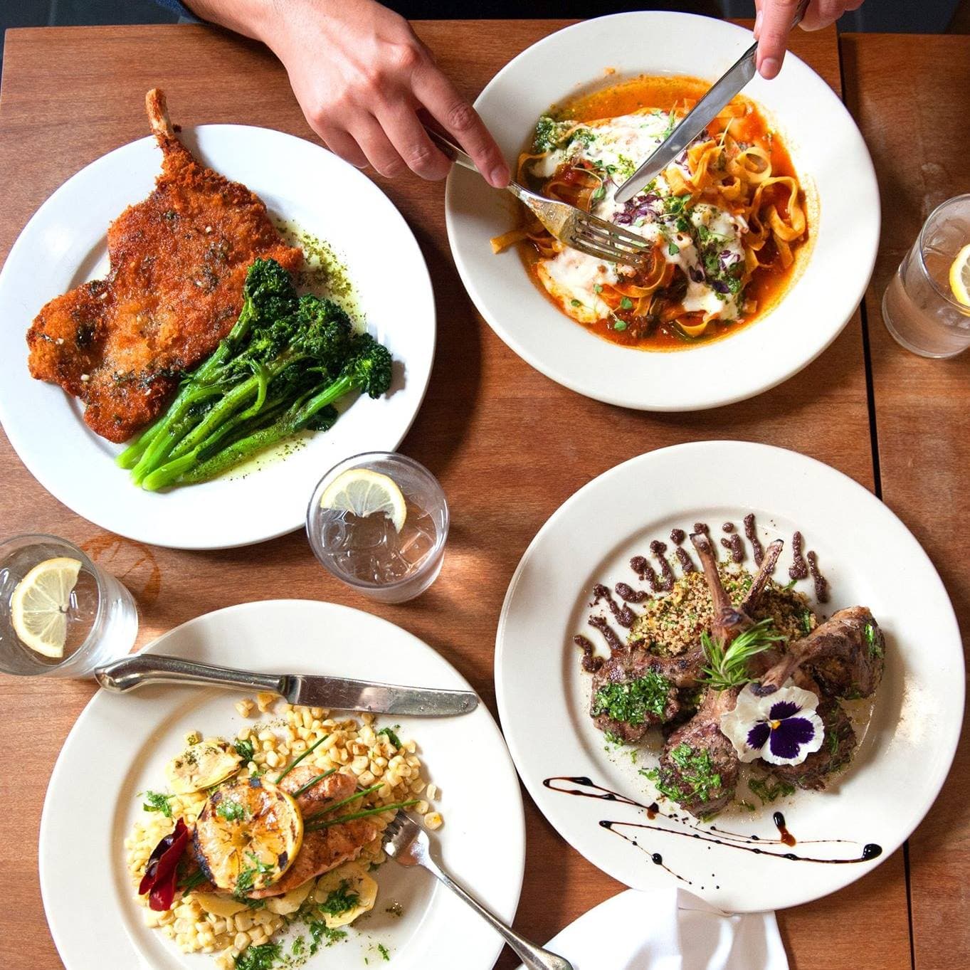 A spread of Caprice plates — pork chop, pappardelle, lamb, and salmon